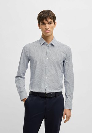 Camicia a maniche lunghe bianca e blu con pattern, colletto button-down, tessuto morbido e design aderente. Abbinata a pantaloni scuri e cintura.