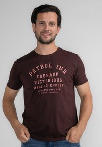 Tmavě burgundské tričko vyrobené z bavlny s krátkými rukávy. Obsahuje tištěný text ve světle růžové barvě, včetně geografických souřadnic a frází.