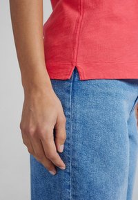 T-shirt di cotone corallo con maniche corte e fessure laterali, abbinato a jeans denim azzurri chiari con una trama sottile e vestibilità standard.
