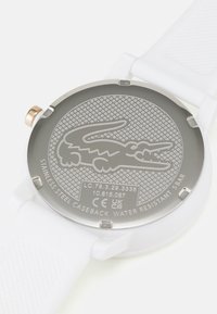 Reloj con correa de silicona blanca y fondo de caja de acero inoxidable, que presenta un diseño de cocodrilo, detalles grabados y una resistencia al agua de 5 bares.