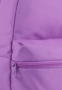 Violet kangasreppu, jossa on teksturoitu pinta, varustettuna vetoketjullisella taskulla ja sileällä vetoketjivarusteella. Lähikuva materiaalin yksityiskohdista.