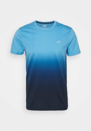 T-Shirt mit kurzem Arm in Blauverlauf, der von einem hellen Blau am oberen Teil zu einem dunklen Marineblau am unteren Rand übergeht, mit einem kleinen Logo auf der Brust.