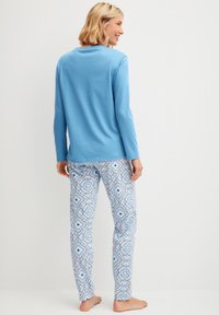 Lichtblauw langmouwen shirt gecombineerd met gemusterde blauwe en witte pyjamabroek met bloem- en geometrische ontwerpen. Zachte stof, ontspannen pasvorm.
