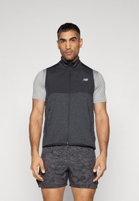 Gilet zippé noir et gris avec un col haut, en matériau léger, et deux poches latérales, porté sur une chemise grise à manches courtes.