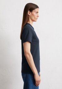 T-shirt blu navy a maniche corte con scollatura a girocollo, realizzato in tessuto morbido. È leggermente aderente in vita, abbinato a jeans blu.