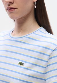 Βαμβακερό μπλουζάκι με ριγέ μοτίβο σε ανοιχτό μπλε, άσπρο και κίτρινο, με στρογγυλή λαιμόκοψη και μικρό κεντημένο πράσινο λογότυπο κροκόδειλου στο στήθος.