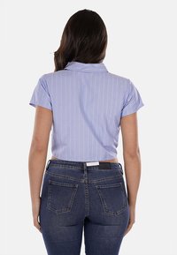 Camisetta azzurro chiaro a cropped con strisce verticali bianche, maniche corte e colletto, abbinata a jeans blu scuro con tasche posteriori.