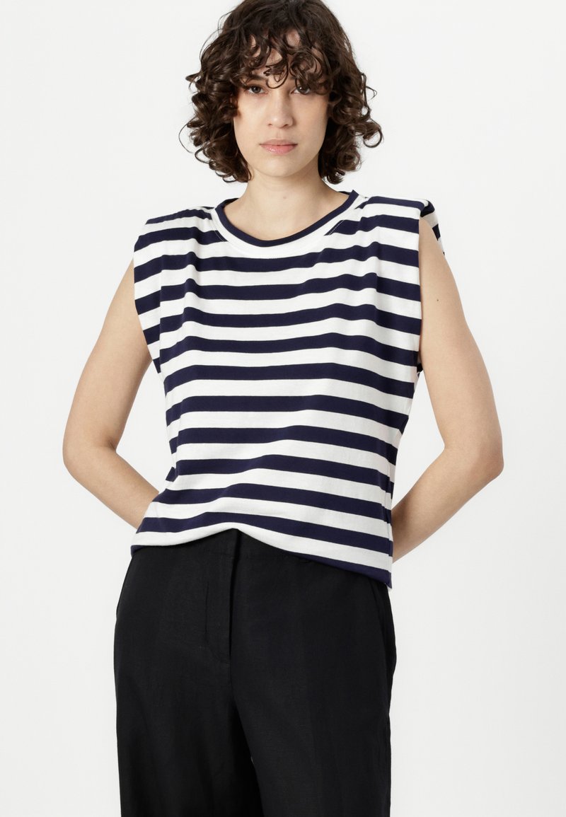 Pas konturowany w niebiesko-białe paski, wykonany z bawełny. Charakteryzuje się okrągłym dekoltem, bezrękawowym krojem z wycięciami na ramionach oraz luźnym fasonem.