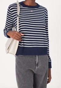 Navy i biały sweter w paski z prążkowanym dekoltem i dołem, w połączeniu z szarymi dżinsami i jasnobeżową torebką na ramię.