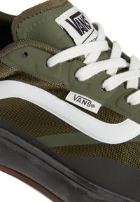 Baskets Vans vert olive avec une bande latérale blanche, des lacets blancs, une semelle noire et le logo Vans visible sur la languette et le côté.