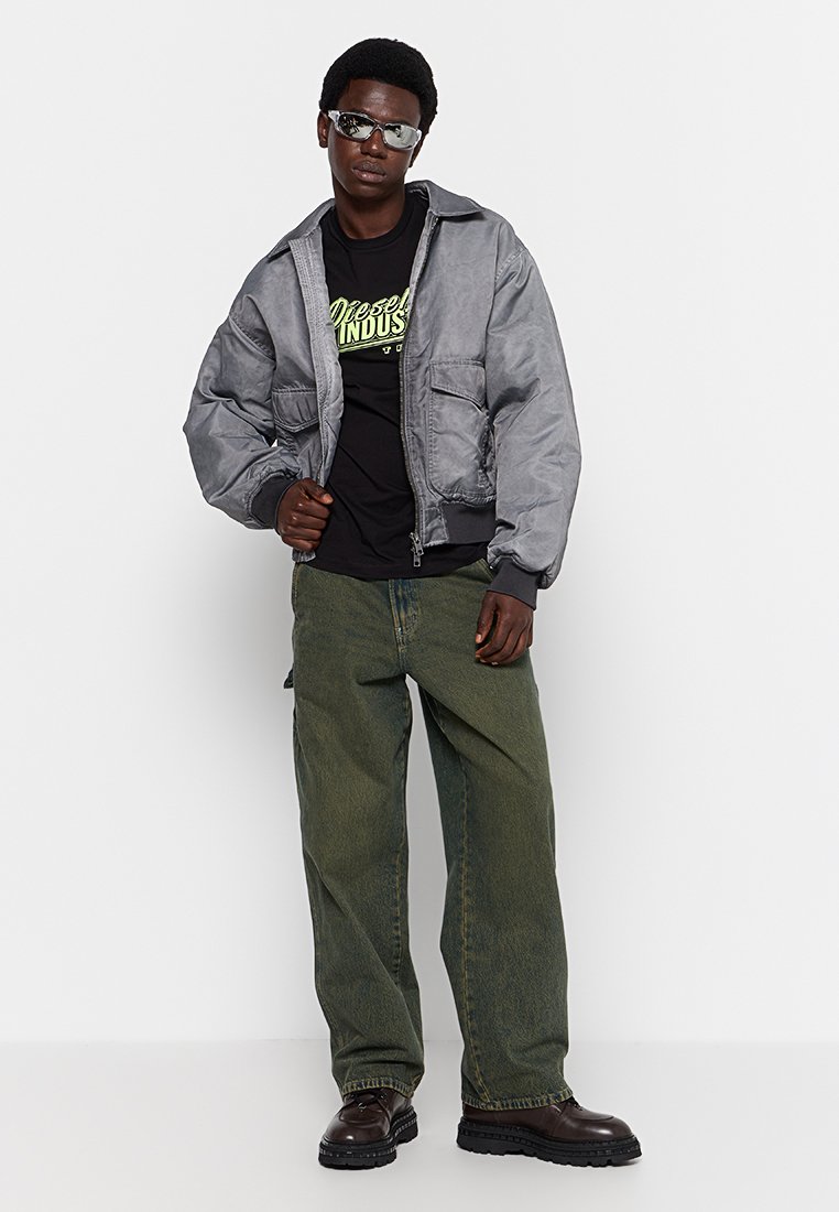 Szara kurtka bombowca z dwoma przednimi kieszeniami, czarna koszulka z neonowym logo, oliwkowe spodnie w szerokim kroju oraz ciemne botki. Gładka faktura materiału.