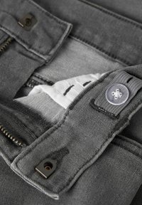 Siv kavčuk jeans z zadrgo in gumbnim zapiranjem, z belim notranjim etiketom in detajli šivov v kontrastni barvi.