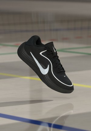 Zwarte sportschoen met witte Nike-swoosh, zwevend boven een gymvloer met gekleurde lijnen voor sportactiviteiten.