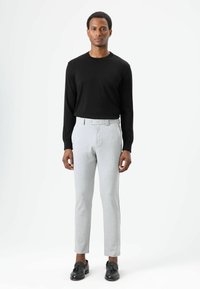 Zwart shirt met lange mouwen en lichtgrijze, op maat gemaakte broek met knoopsluiting en een slanke pasvorm, gecombineerd met zwarte loafers. Minimalistisch ontwerp.