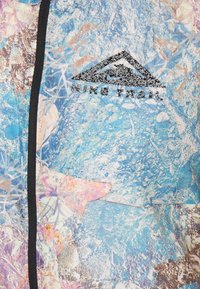 Veste de trail Nike avec un motif abstrait bleu agrémenté d'accents violets et roses, en tissu léger, et une fermeture éclair noire sur le devant.