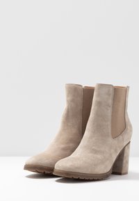 Botas de tobillo de ante beige con un tacón ancho, paneles laterales elásticos y punta redondeada. Acabado texturizado y suela de goma para mayor agarre.