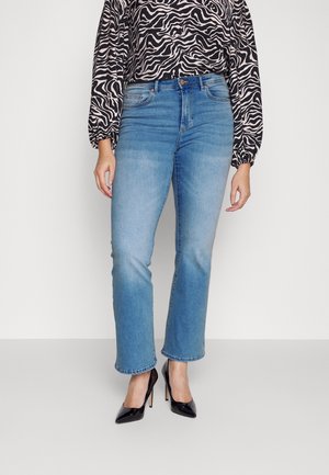 Vrouw draagt lichtblauwe rechte jeans, zwarte lakleren hoge hakken en een lange mouwen blouse met zwart-witte zebra print.