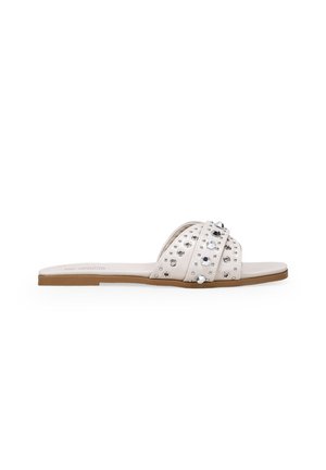 White slide sandals with two crisscross straps, embellished with silver studs and gemstones, flat sole, and a smooth texture.