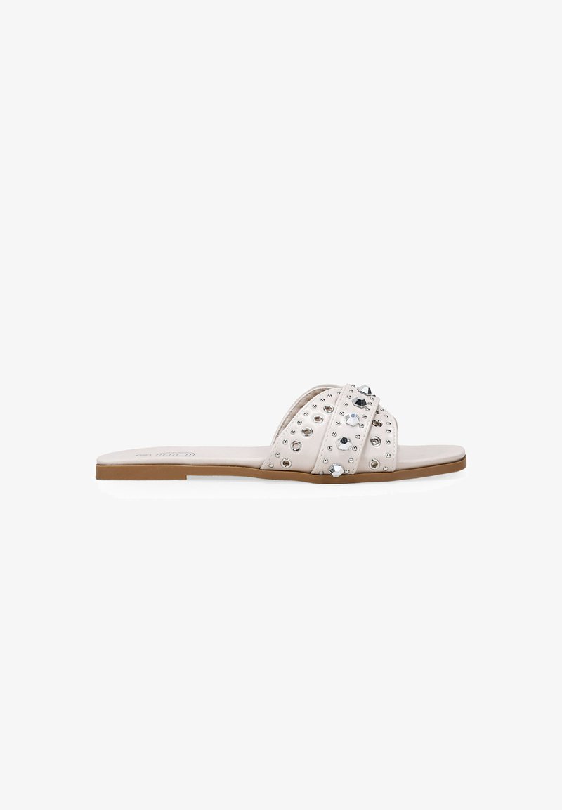 White slide sandals with two crisscross straps, embellished with silver studs and gemstones, flat sole, and a smooth texture.