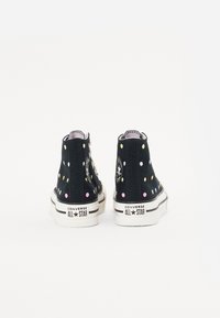 Zwart canvas hoge sneakers met kleurrijke stippen, witte rubberen zool met zwarte strepen, en Converse All Star branding op de hiel.