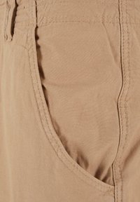 Beige fabric shorts with a side pocket, featuring a soft texture and visible stitching along the seams. Casual design for comfort.