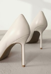 Korkokengät pehmeää beigeä nahkaa, joissa on terävä kärki ja kapea stiletto-korko. Sujuva pinta ja minimalistiset muotoiluelementit.