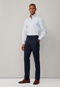 Camisa de dress de rayas azul claro con cuello, botonera y mangas largas, combinada con pantalones oscuros de color azul marino y zapatos de cuero marrón.
