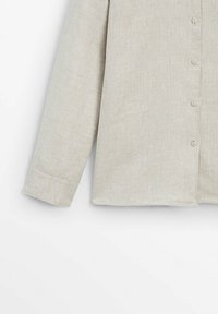 Chemise beige clair à manches longues avec un devant boutonné et une seule manchette sur un fond blanc uni.
