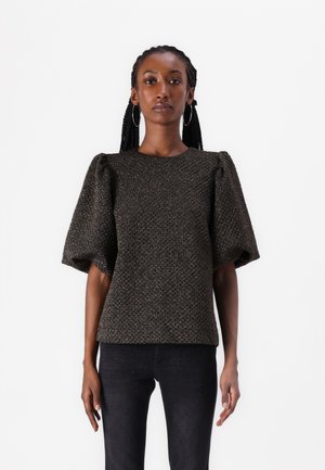 Textured, dark woven top with puffed sleeves, round neckline, and a subtle pattern. Paired with fitted, dark jeans featuring studded accents.