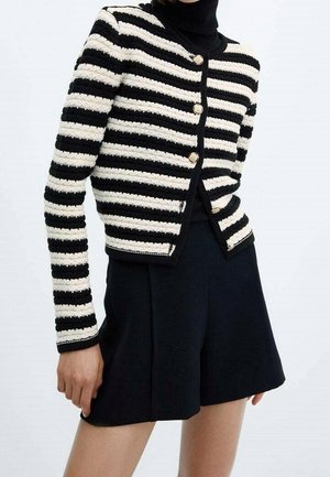 Schwarz-weiß gestreifte Strickjacke mit Knöpfen, horizontal gestreift, getragen über einem schwarzen Rollkragenpullover, kombiniert mit einem hoch taillierten schwarzen Rock.
