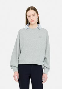 Sweatshirt gris au design court, avec un col rayé bleu et blanc. Manches oversize avec une bordure côtelée et un détail de logo.
