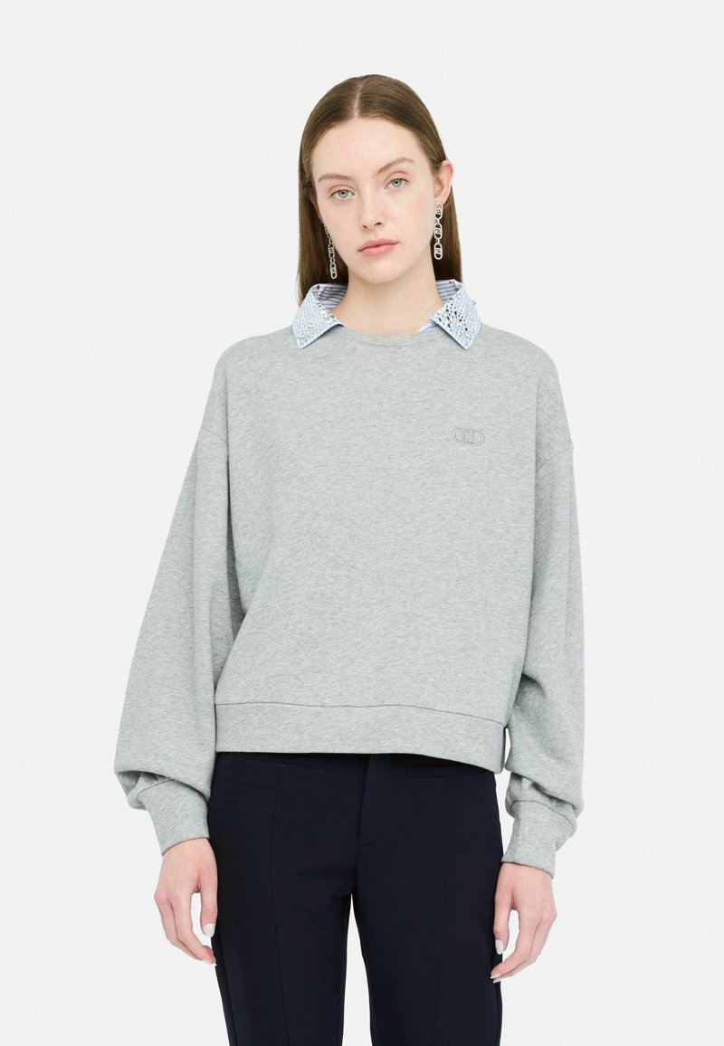 Grijze sweatshirt met een cropped ontwerp, voorzien van een blauw-witte gestreepte kraag. Overmaatse mouwen met een ribgebreide zoom en logodetail.