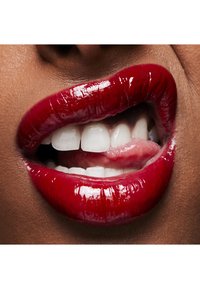 Des lèvres brillantes et rouges, avec une texture lisse, révélant des dents blanches. La langue est visible entre les lèvres, accentuant la forme de la bouche.
