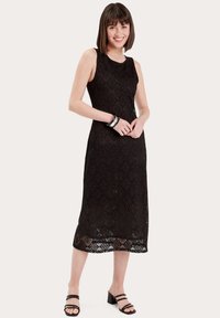 Robe midi en dentelle noire avec une texture à motifs, design sans manches, et un ourlet doté d'une finition en dentelle détaillée. Associée à des talons noirs à lanières.