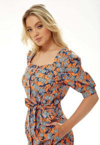 Orange floral dress featuring puff sleeves, a square neckline, and a belted waist. The fabric displays blue and white daisy patterns.
