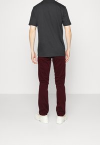 Pánské tmavě šedé tričko s krátkým rukávem v kombinaci s vínovými kalhotami. Bílé tenisky viditelné, ukazujícasual outfit zezadu.