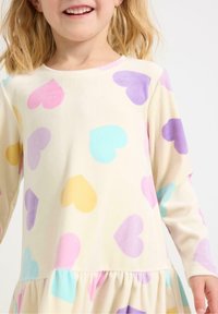 Langærmet kjole i blødt stof med en cremefarvet baggrund og farverige hjerte mønstre i pink, lilla, gul og blå. Flæser nederst.