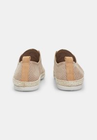 Light beige shoes with perforated texture, suede accents, and woven jute soles; features a tan tab at the heel for easy wear.