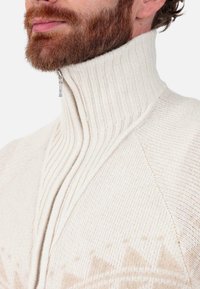 Pull en maille écru avec un col montant côtelé et une fermeture à moitié zippée. Présente un tissu texturé et des motifs géométriques subtils près de l'ourlet.
