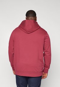 Bordowa bluza z kapturem z kieszenią kangurka i regulowanym sznurkiem. Posiada ściągacze przy rękawach i na dole, wykonana z miękkiego, teksturowanego materiału.