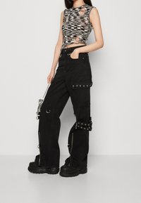 Pantalones cargo negros con múltiples bolsillos con cremallera y acentos de metal. El top corto presenta un patrón en zigzag blanco y negro con recortes.