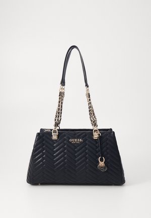 Schwarze gesteppte Handtasche mit goldenen Kettenriemen, GUESS-Logo und dekorativen goldenen Anhängern, die an einer Seite hängen.