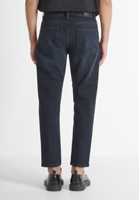 Jeans de mezclilla azul oscuro con un corte ajustado, cinco bolsillos y una cinturilla clásica. La tela tiene un acabado suave y ligeramente texturizado.