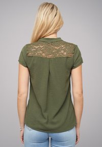 Haut olive à manches courtes avec un panneau arrière en dentelle, col rond et coupe décontractée. Tissu doux avec une légère texture, design décontracté.