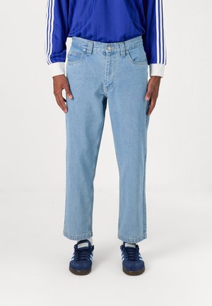 Light blue straight-leg jeans made of denim. Features five pockets, a button closure, and visible stitching. Worn with dark blue sneakers.