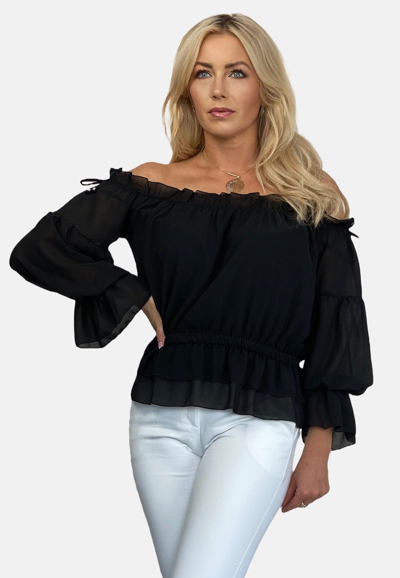 Czarna bluzka bez ramiączek z falbaniastymi rękawami i elastycznym pasem, o zwiewnym fasonie i przezroczystej strukturze. W zestawie z białymi spodniami.