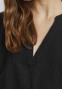 Top in lino nero con scollatura a V. Il tessuto ha una texture liscia e il design presenta una vestibilità comoda con dettagli di cucitura minimi.