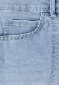 Tissu en denim bleu clair en gros plan montrant une poche avant avec une couture jaune et une passants de ceinture sur le côté droit.