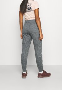 Gray, tapered sweatpants with a textured fabric. Back view shows an elastic waistband and subtle stitching accents. Worn with burgundy shoes.