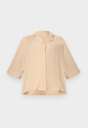 Μπεζ, άνετη, υφασμάτινη πουκάμισα με κουμπιά, με μανίκια μέχρι τον αγκώνα, μικρό γιακά και μια τσέπη στο στήθος, σε απλό φόντο.